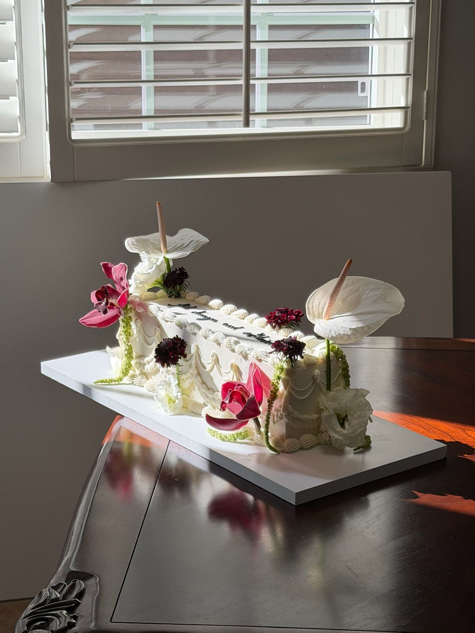 Long piped sheet cake with anthuriums and orchids on a dark polished dining table