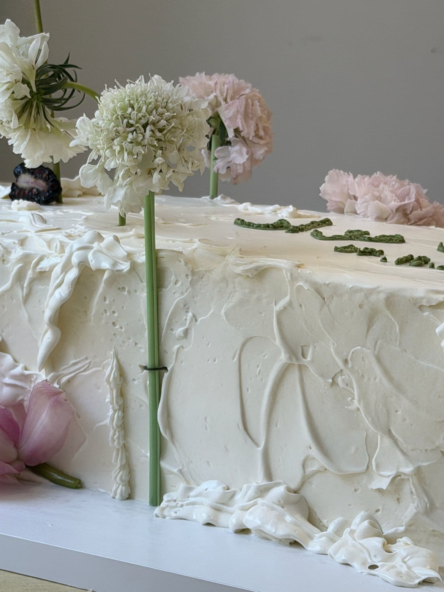 Detail of a long buttercream sheet cake with green lettering and flowers on stems