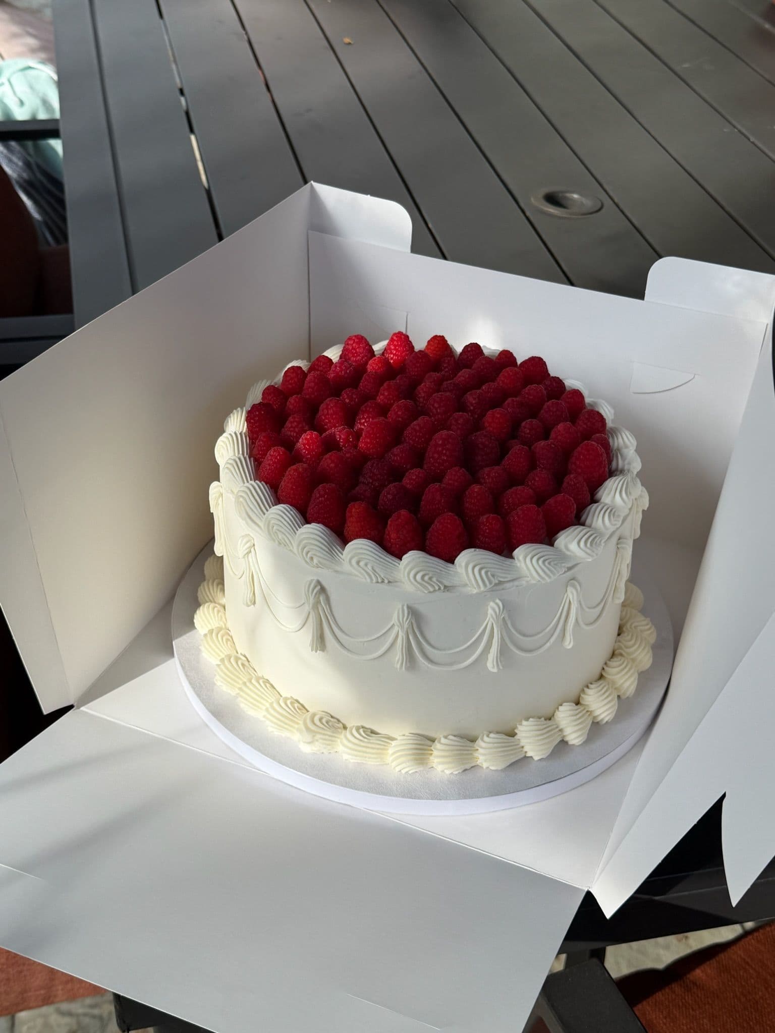 Raspberry-topped vintage piped cake with swag detail, boxed for pickup