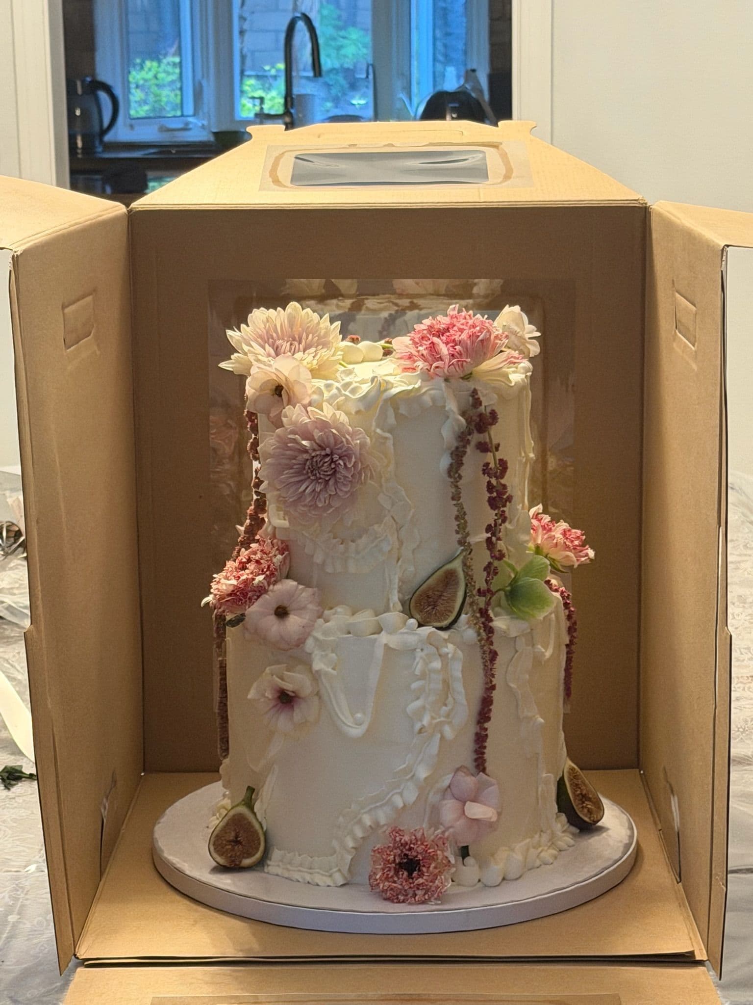 Two-tier textured cake with dusty pink blooms and piped detail, boxed for transport