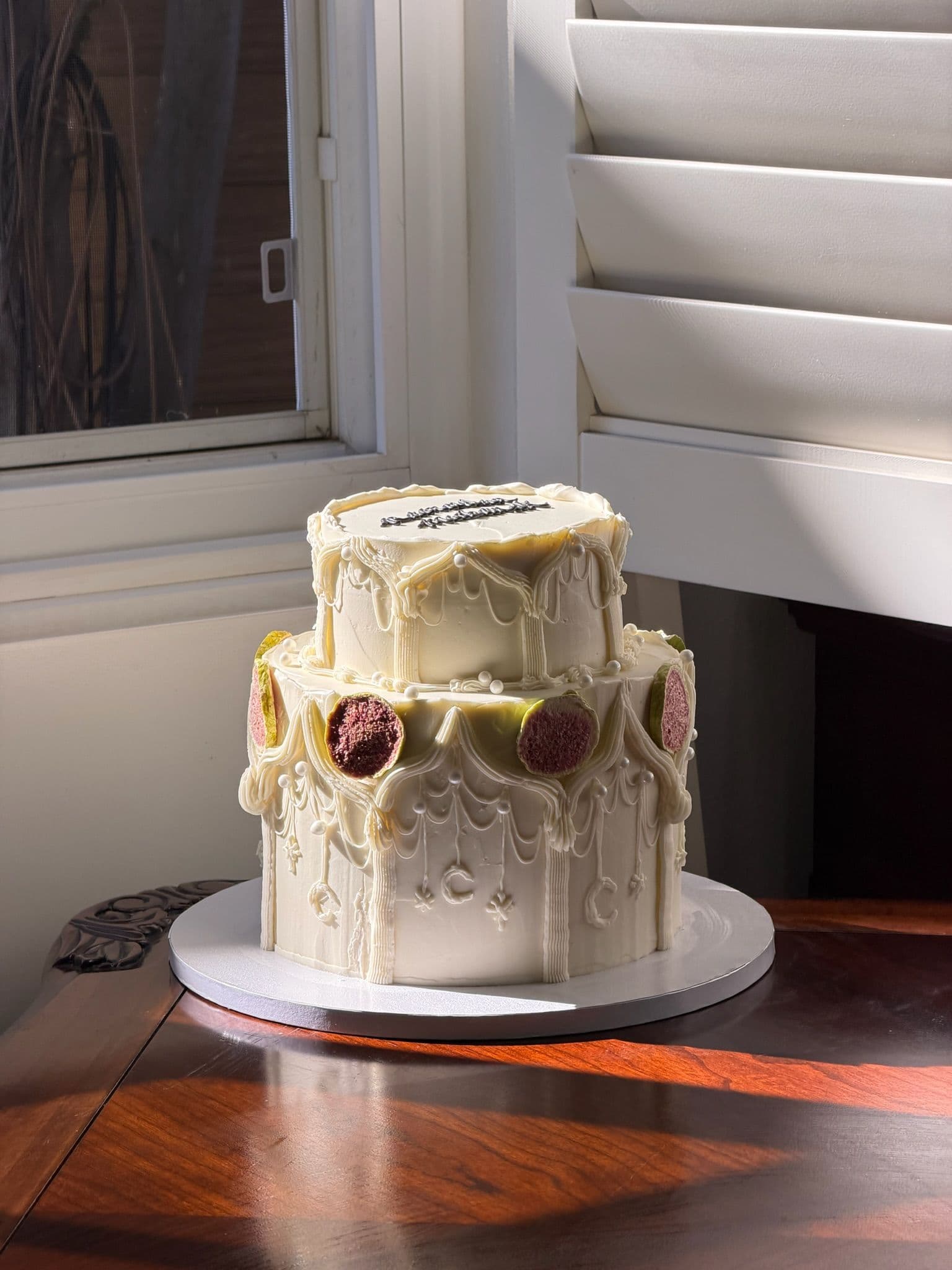 Two-tier cake with baroque piped ruffles and berries, on a warm wood table