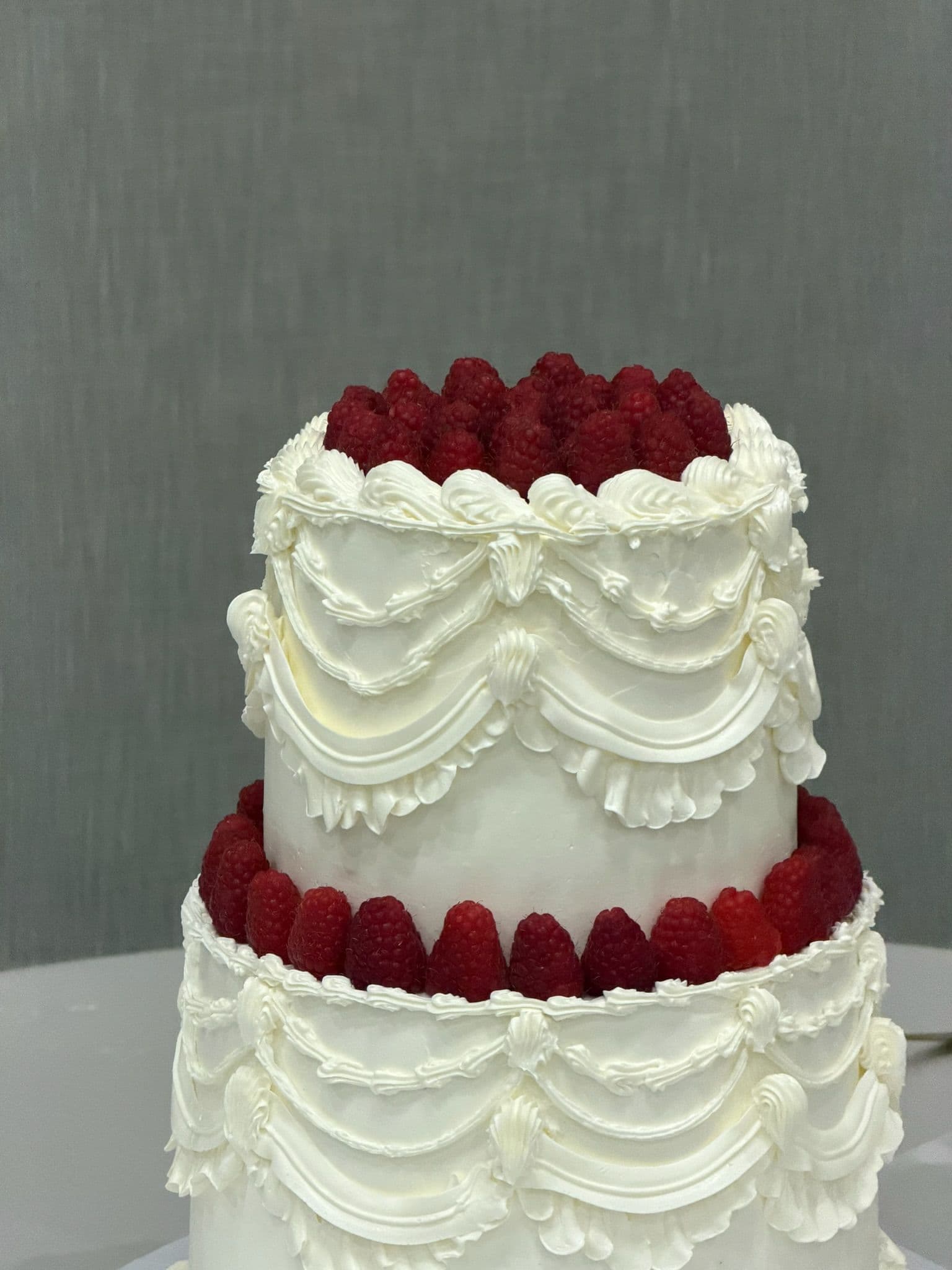 Close view of piped buttercream swags between two raspberry-crowned tiers