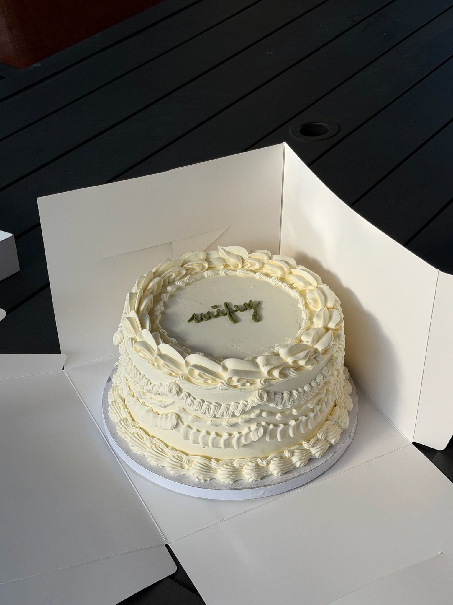 Round cake with layered piped ruffle borders and "wifey" lettered in green