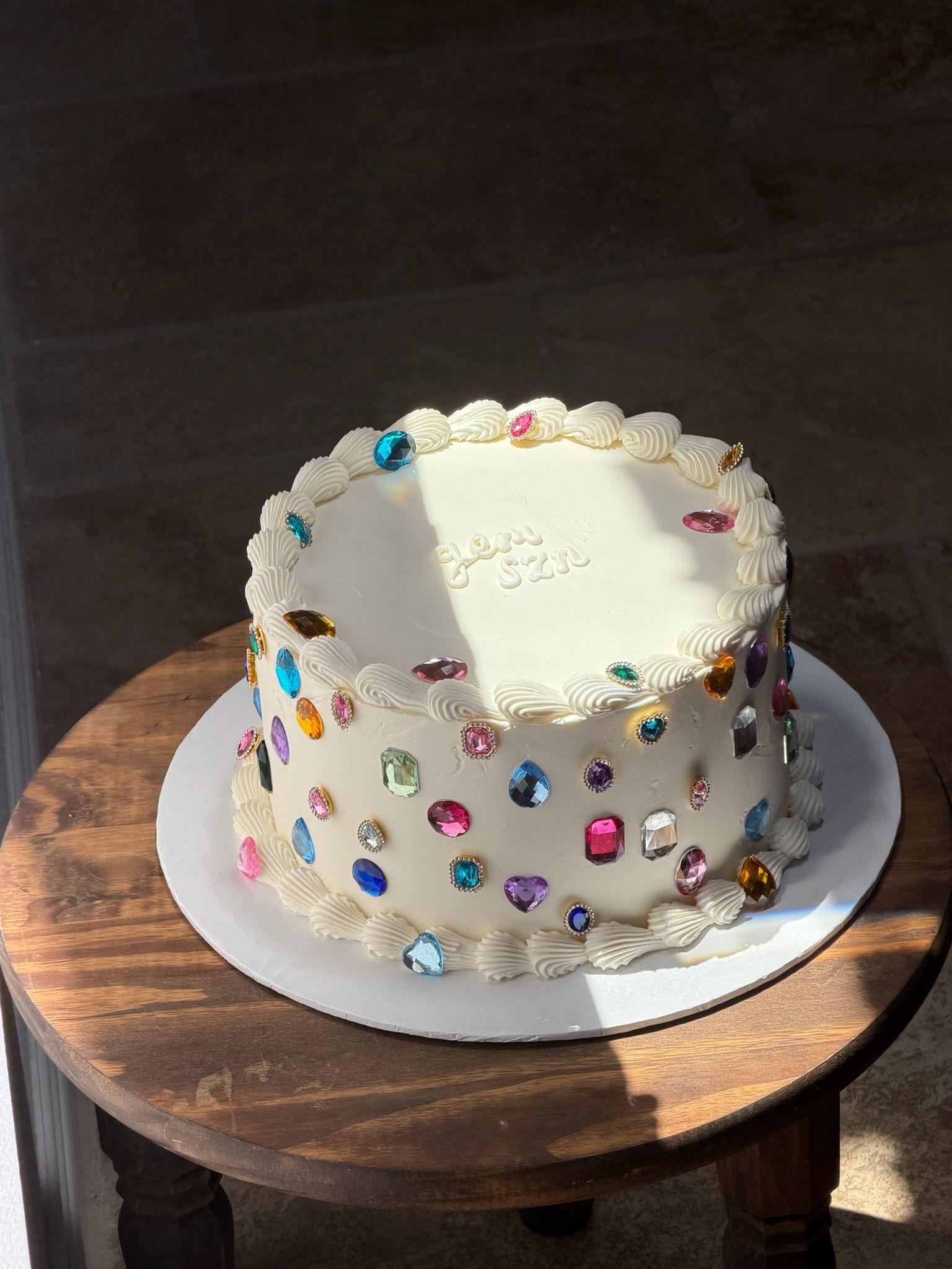 White cake studded with colorful candy gems and "gem szn" piped on top