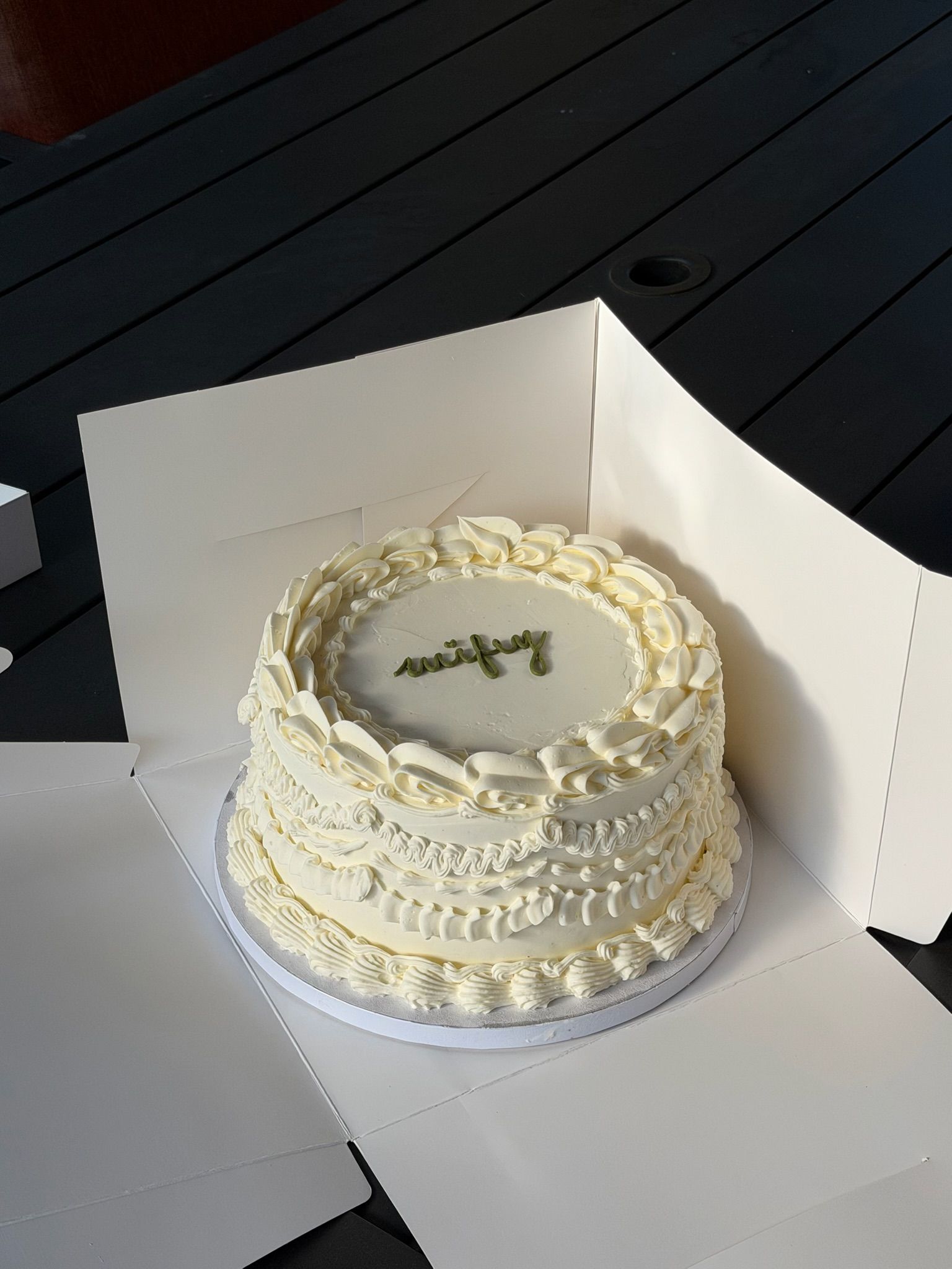 Round cake with layered piped ruffle borders and "wifey" lettered in green